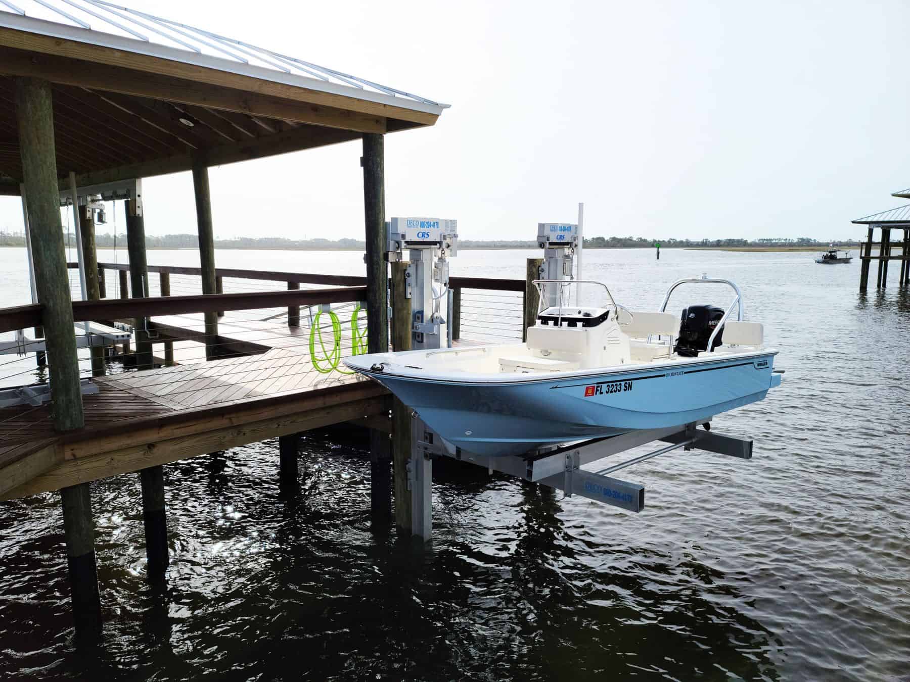 Light blue center-console boat raised on an aluminum lift beside a covered dock