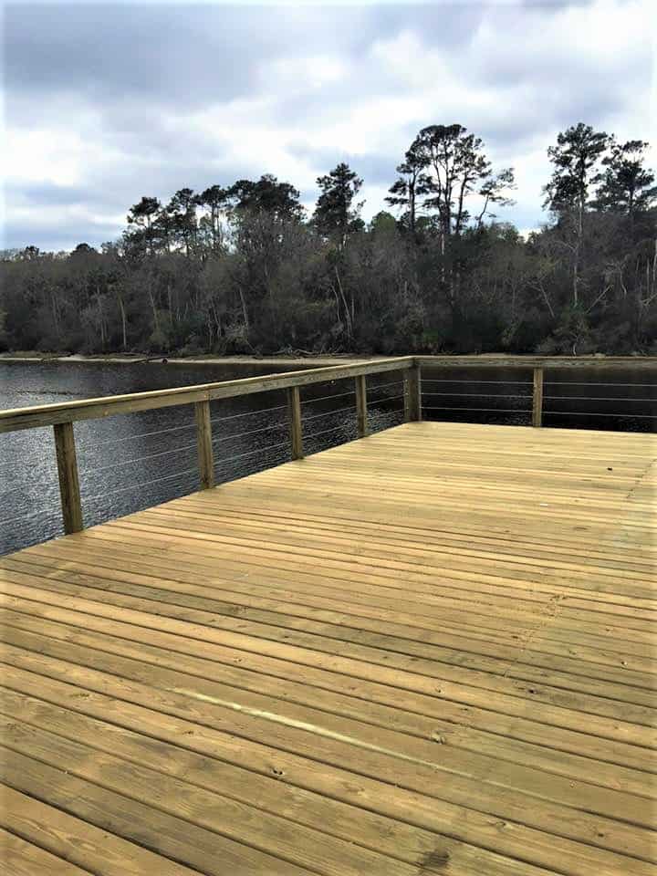 Fresh pressure-treated dock platform with wood posts and cable railing over a wooded river