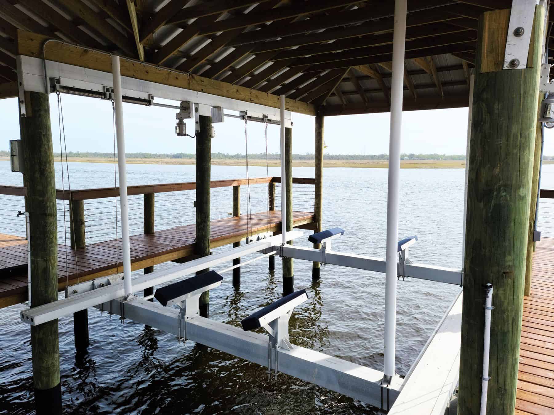 Empty aluminum boat lift with padded bunks under a wood boathouse roof over open water