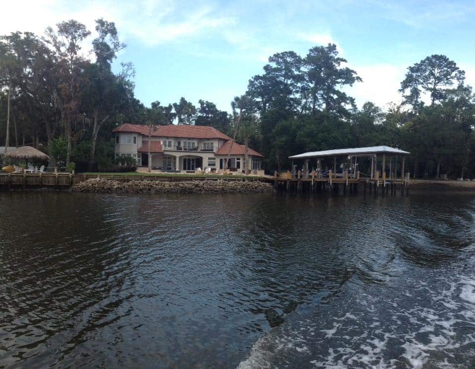 View from the water of a riverfront home with covered boat dock and rock-lined shoreline