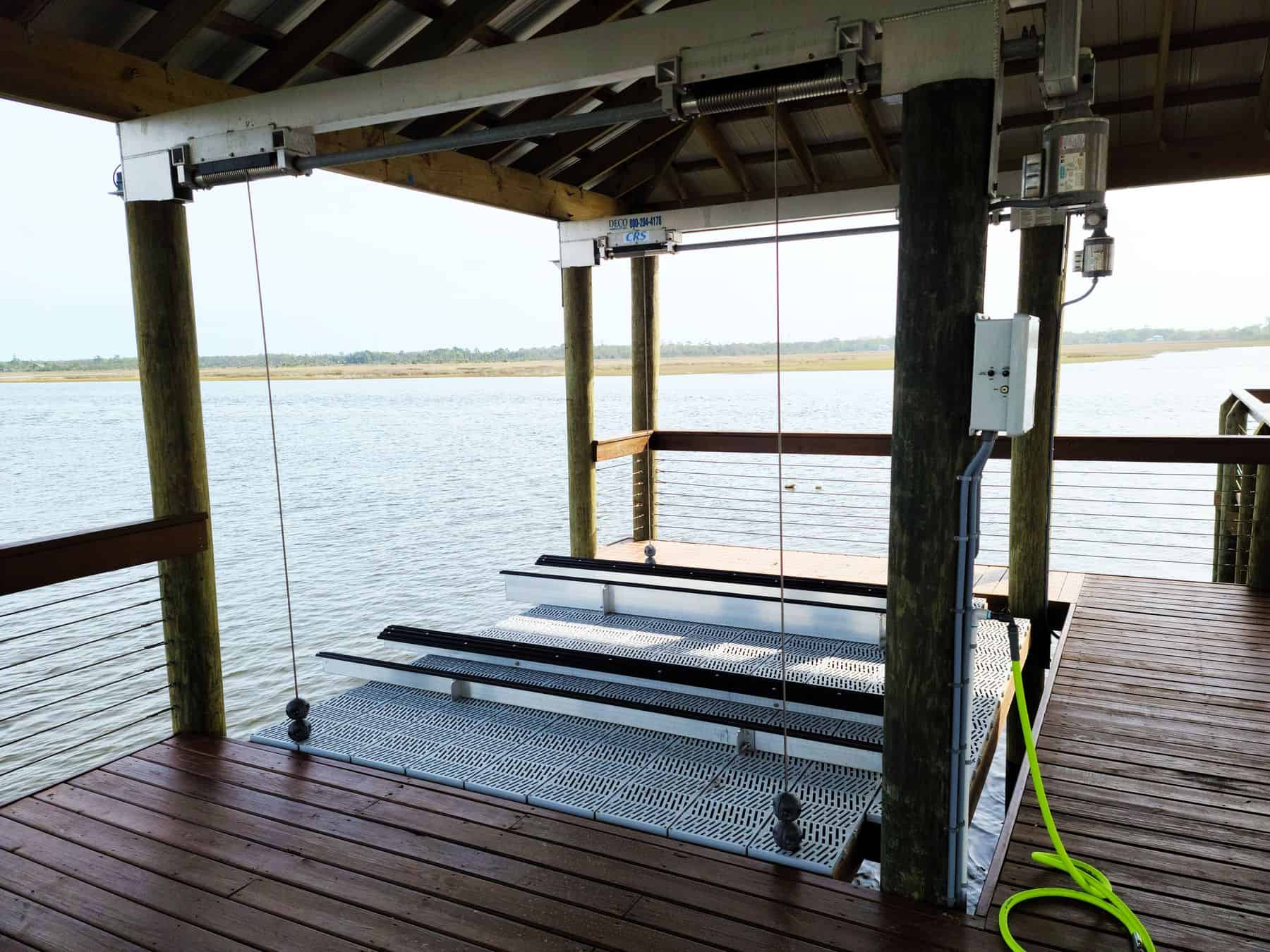 Aluminum boat lift cradle with grated platform raised beside a stained wood covered dock