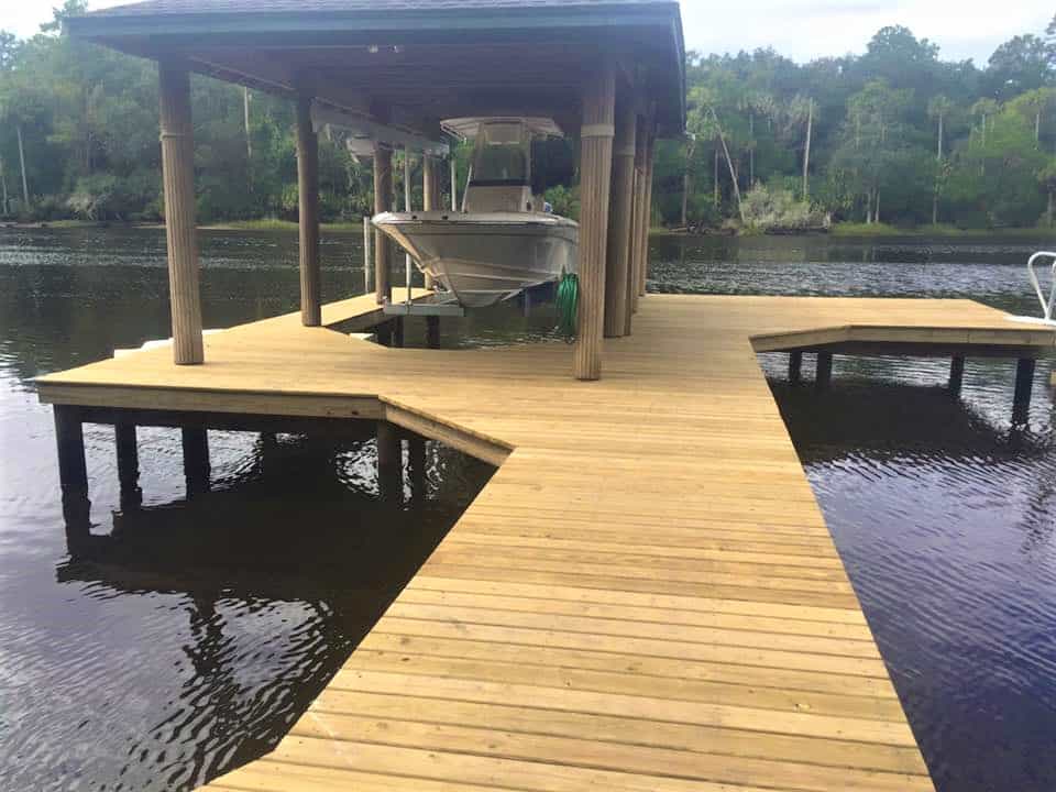 New wood dock with angled walkway leading to a covered slip holding a center-console boat
