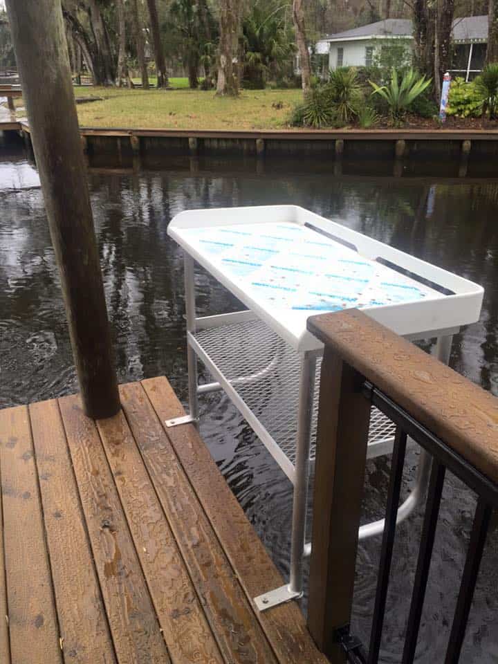 White fish-cleaning table mounted on a dock rail above a canal, bulkhead across the water