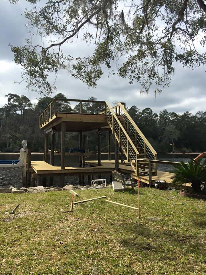Two-story wood dock with upper sun deck, stair run and boat slip on a river shoreline