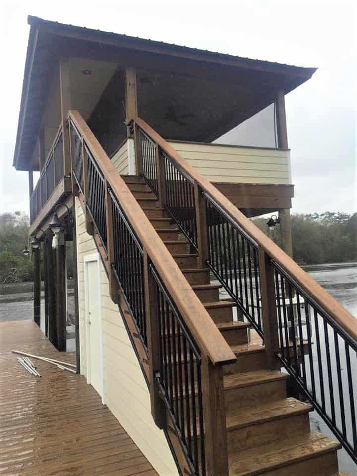Stained stair run with black metal balusters climbing to a covered upper deck on a boathouse