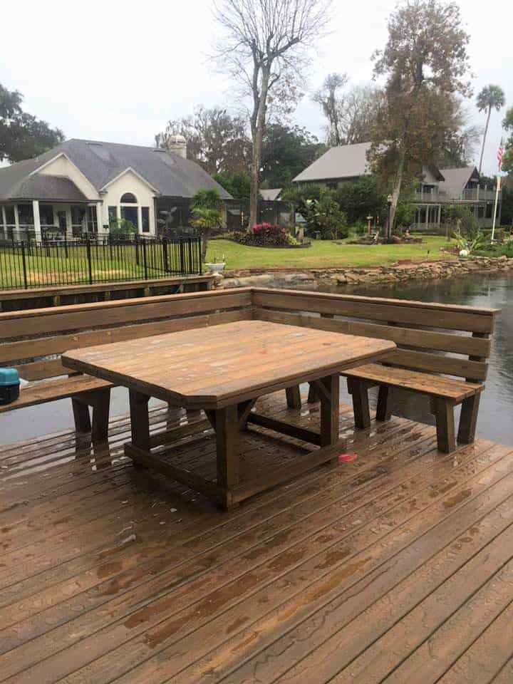 Wood picnic table and built-in bench seating on a rain-wet dock deck facing waterfront homes