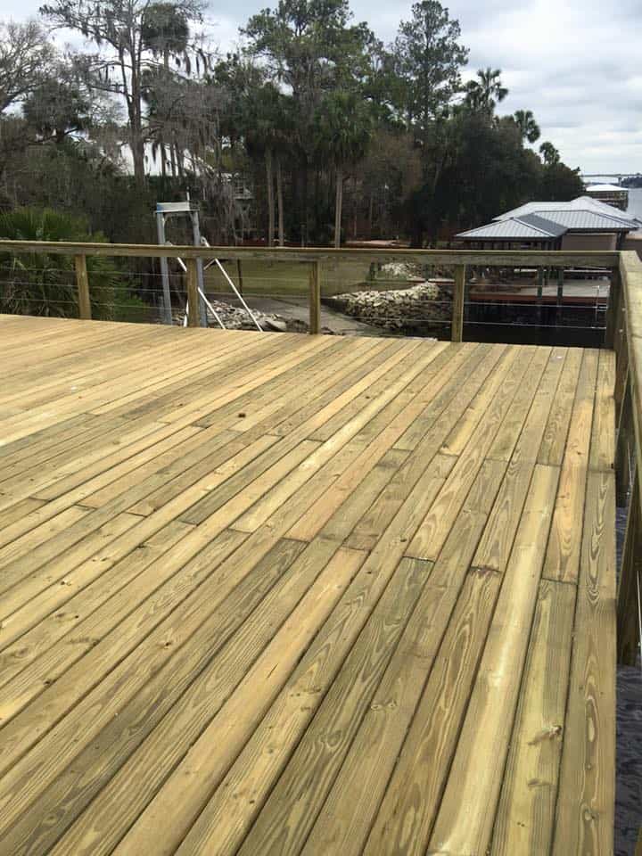 Wide new pressure-treated dock deck with cable railing, covered dock and rock bank beyond