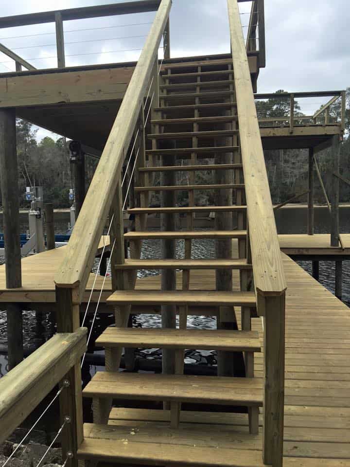 Wood stair run with handrails rising from a dock deck to an upper platform over the water