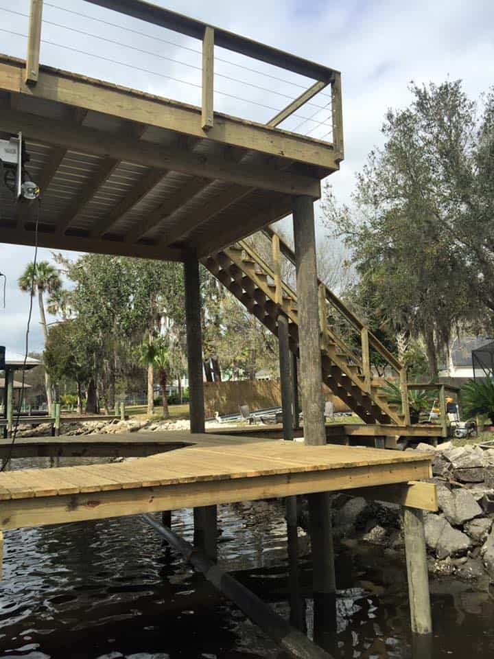 Elevated dock deck on pilings with stairs down to a lower platform and riprap shoreline