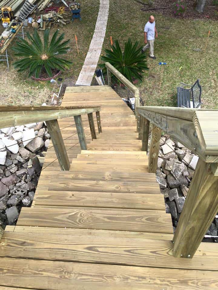 Looking down a new wood stairway from a dock toward a yard where a man walks