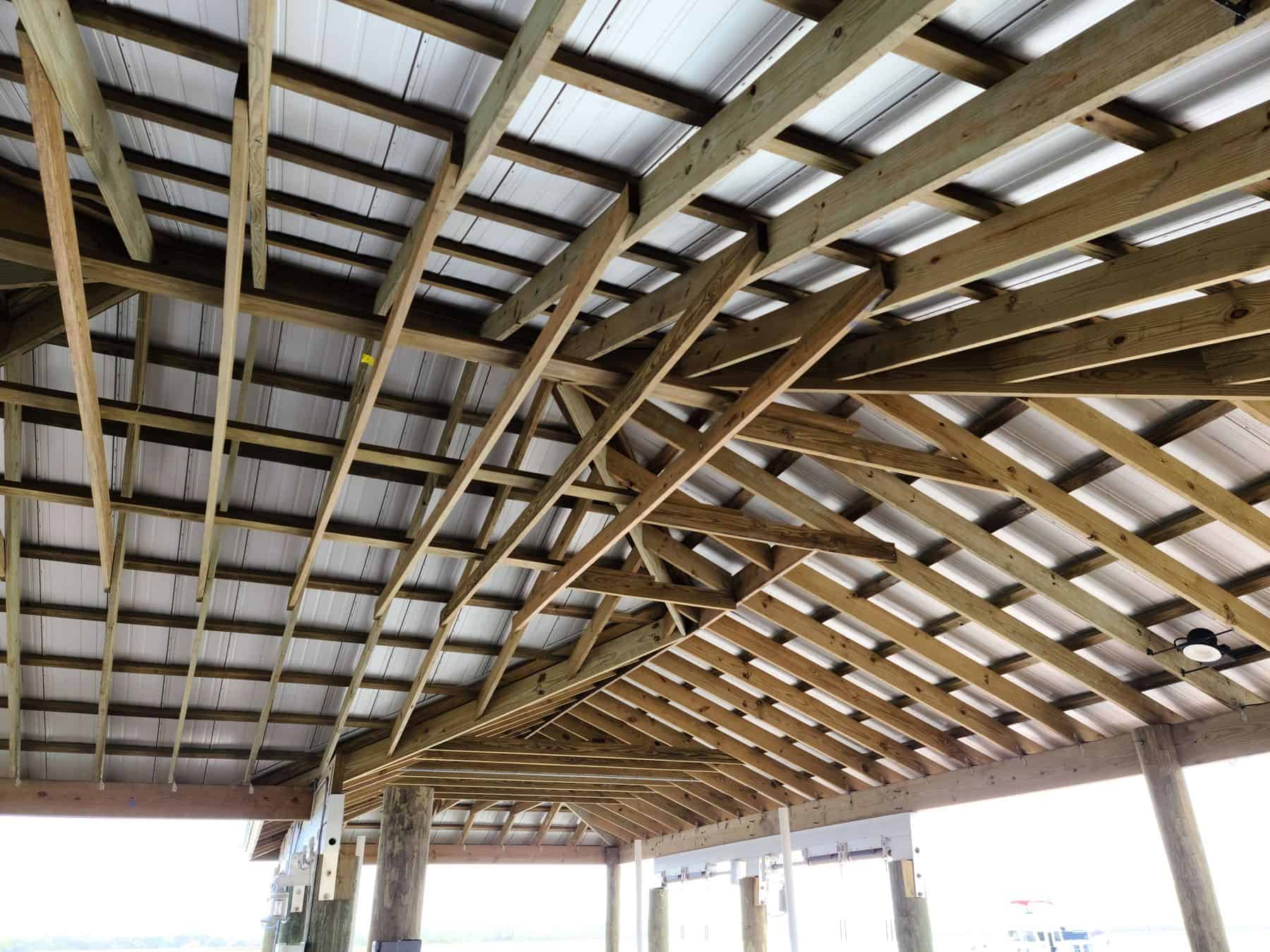 Underside of a large boathouse roof, wood rafters and hip framing under white metal panels