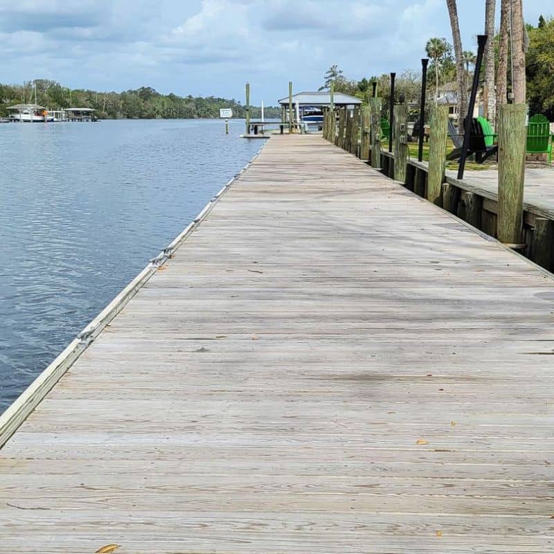 Long weathered wood dock walkway beside a river, covered dock and boat at the far end