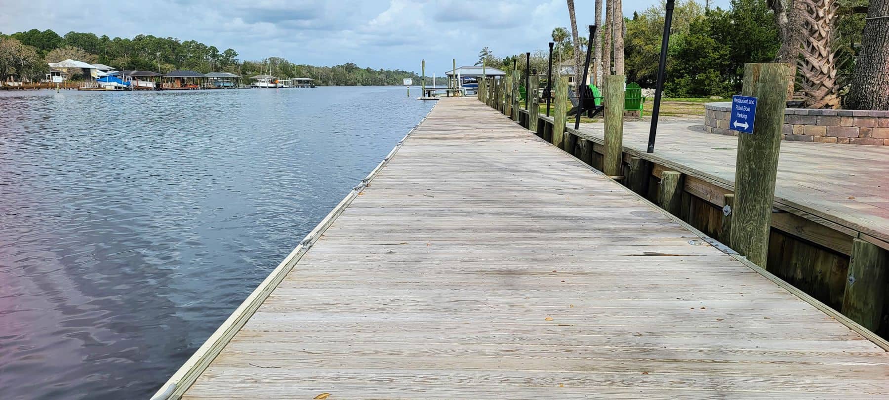 Wide riverfront boardwalk dock with pilings, lamp posts and boat parking sign along the bank