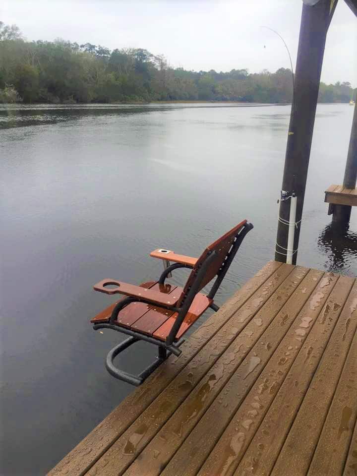 Wooden swivel chair with cup holders mounted at the edge of a rain-wet riverfront dock