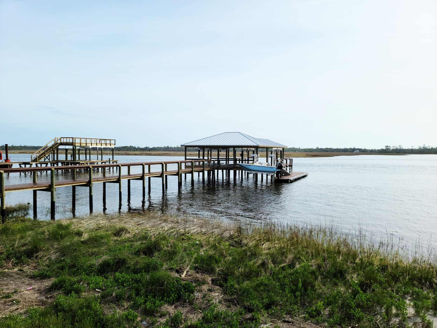 Metal-roofed covered boathouse at the end of a marsh pier, with observation deck and stairs
