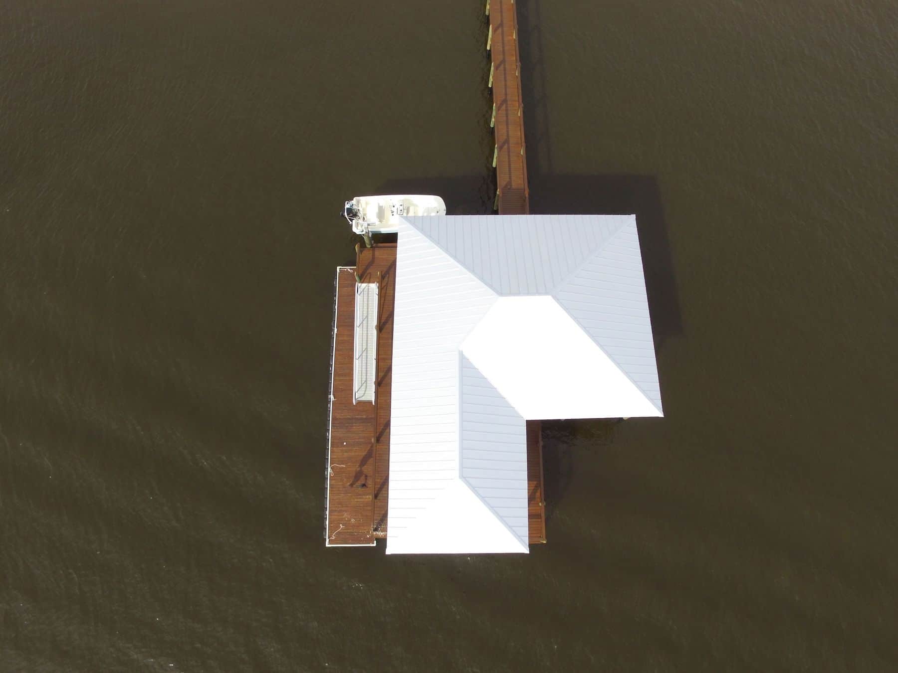 Straight-down aerial of a white metal boathouse roof with adjoining dock walkway and moored boat