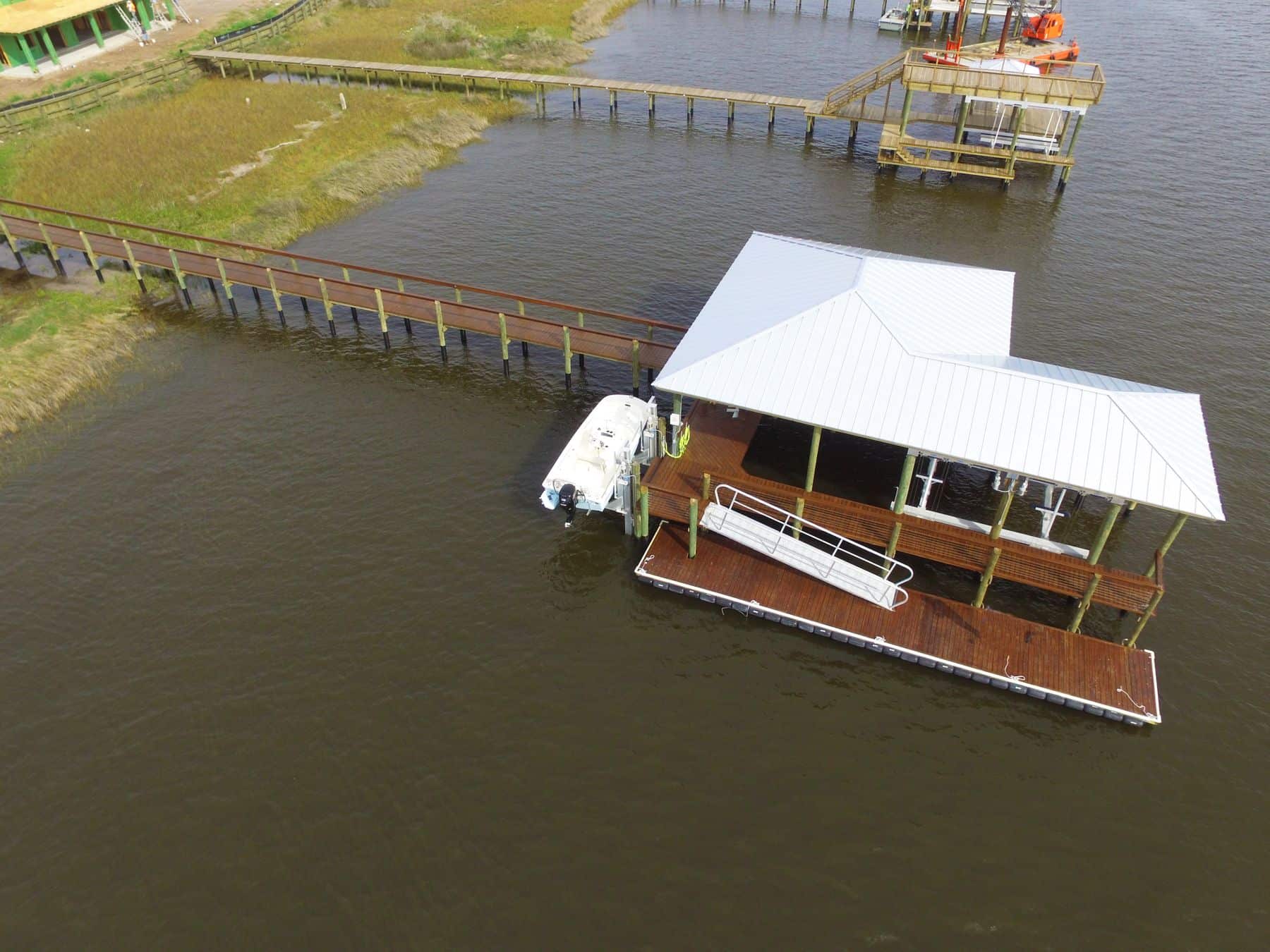 Aerial of a covered boathouse, floating dock and aluminum gangway at the end of a long pier
