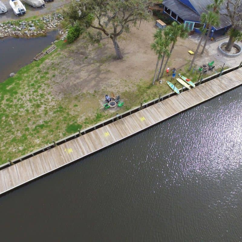 Aerial of a long timber bulkhead capped with a walkway along a lawn beside dark river water