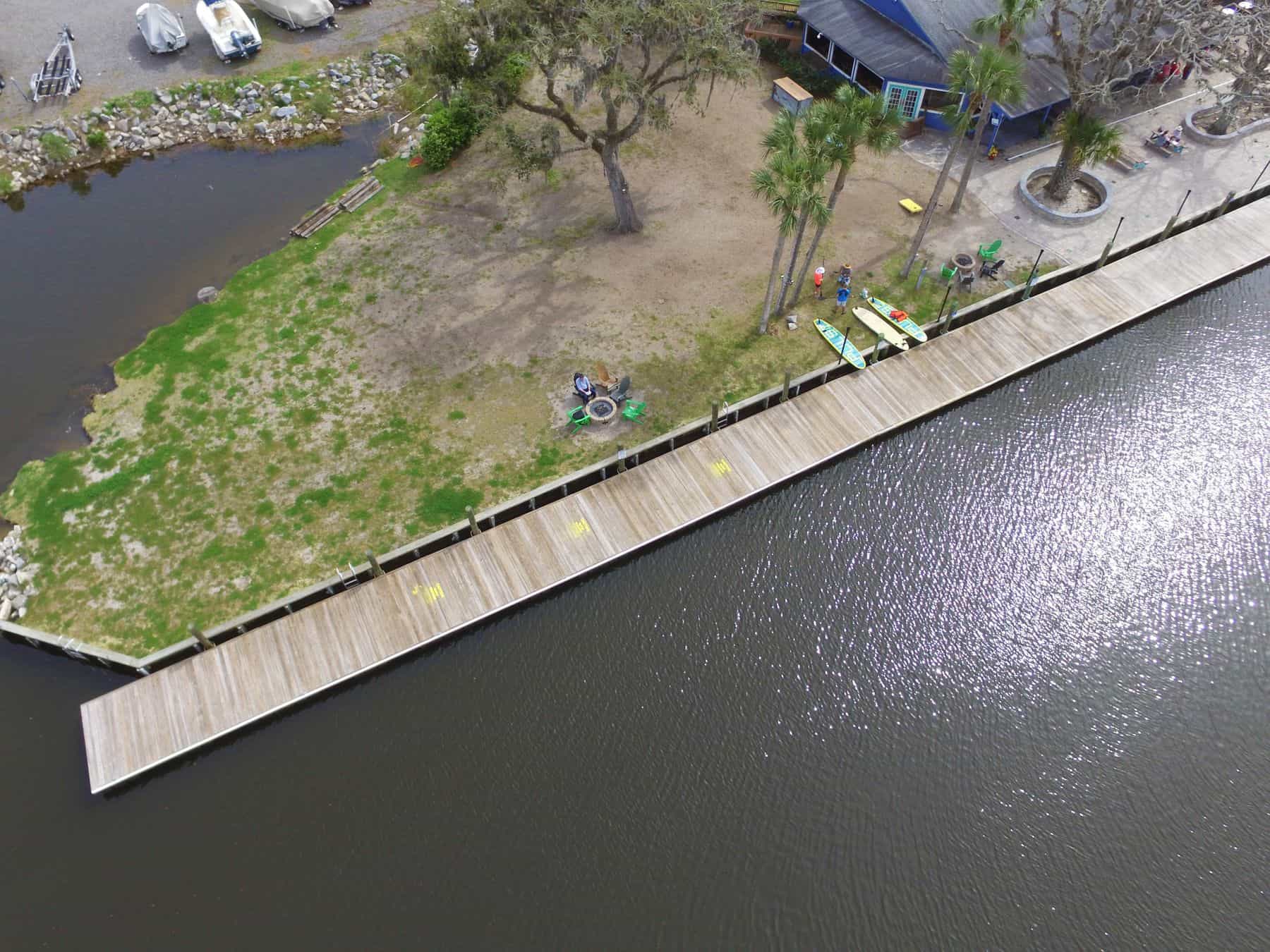 Aerial of a long timber bulkhead and walkway lining a riverbank with paddleboards staged ashore