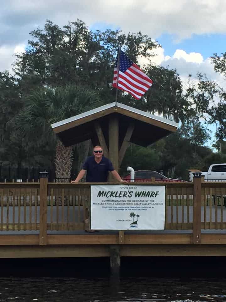 Man standing at a wharf railing beneath a timber pavilion with a Mickler's Wharf banner