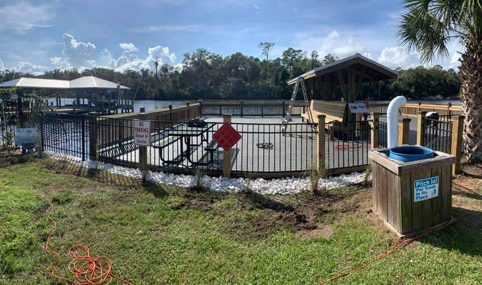 Fenced waterfront deck with picnic table and pavilion beside a river and a covered boathouse