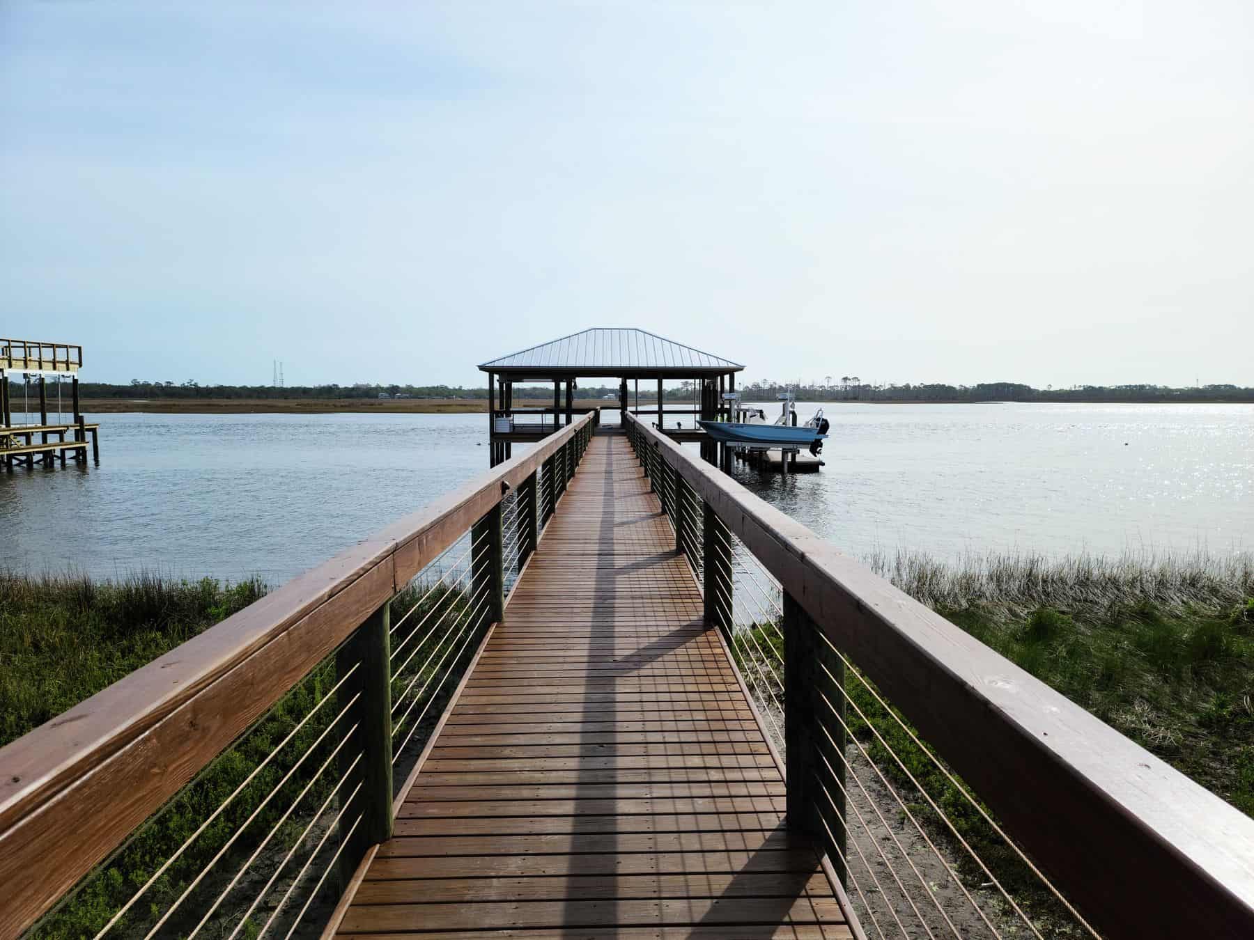 Wood pier with cable railing running out to a covered boathouse and moored boat