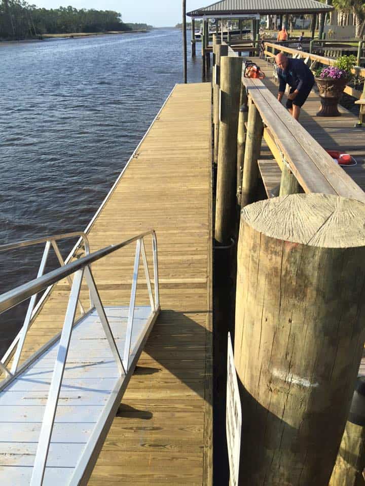 Wood dock with aluminum gangway and heavy pilings alongside a raised riverfront deck where a man works