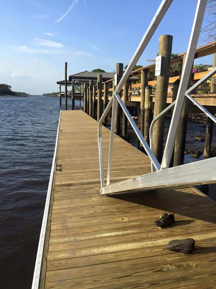 Wood dock walkway with aluminum gangway beside pilings and a raised covered riverfront structure
