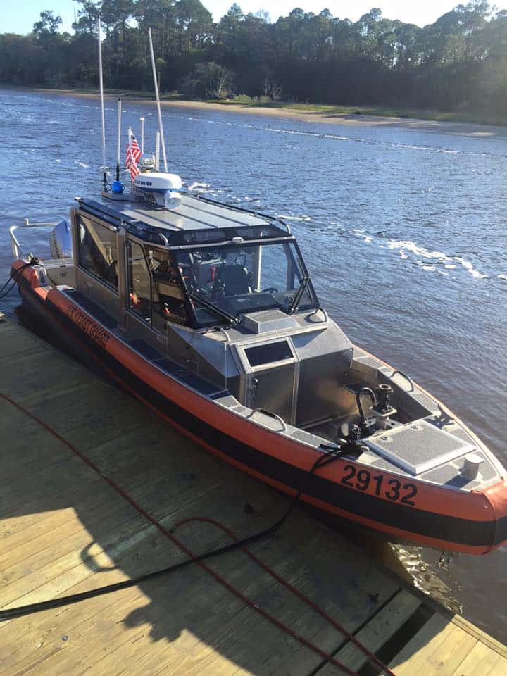 Orange and grey Coast Guard response boat tied alongside a weathered wood dock on a tidal river