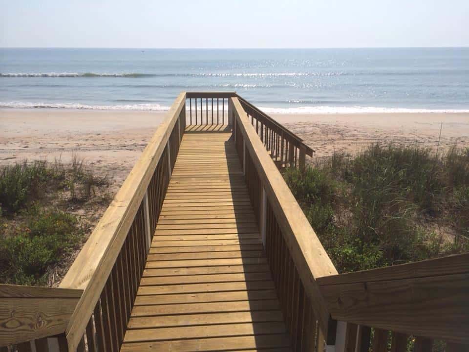 Wooden boardwalk with railings running over dune vegetation toward the beach and ocean