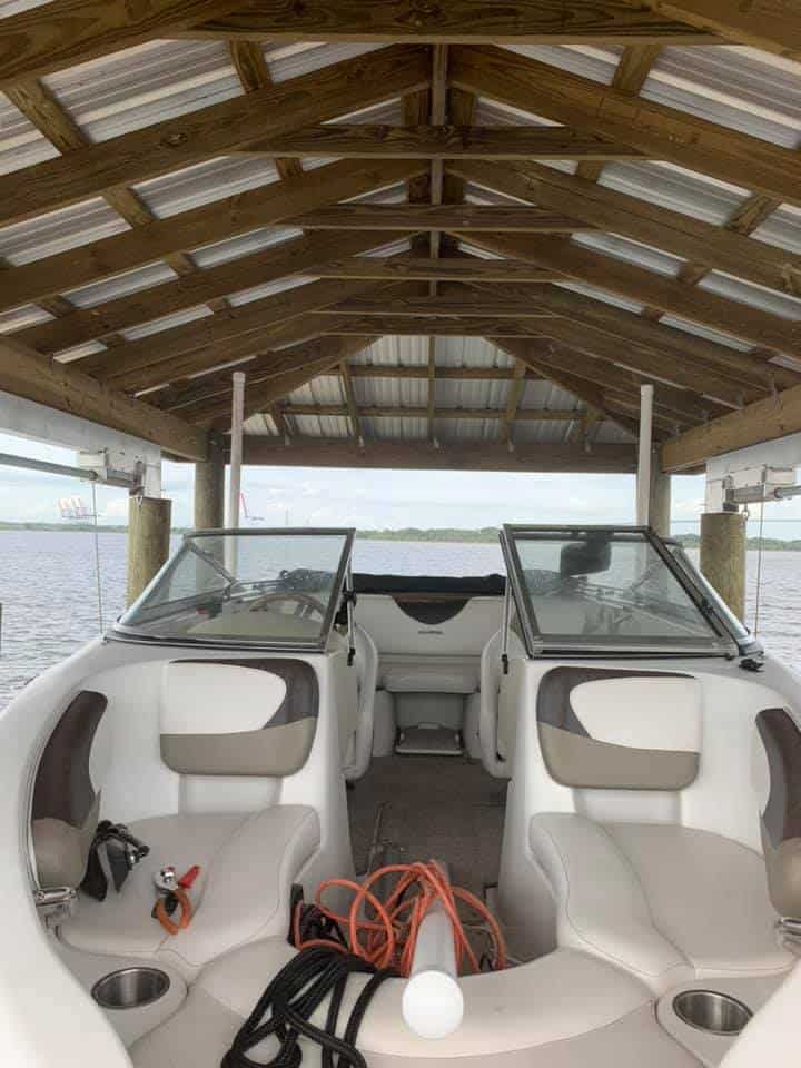 Cockpit view from a white bowrider under a wood-truss boathouse roof, water beyond the bow