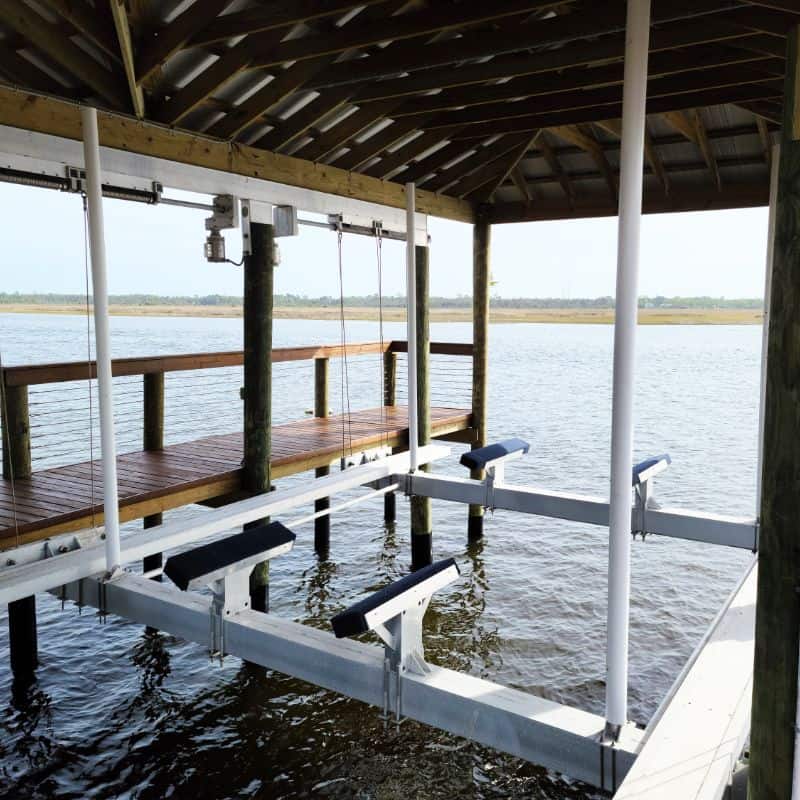 Empty aluminum boat lift with padded bunks under a boathouse roof, water and marsh beyond