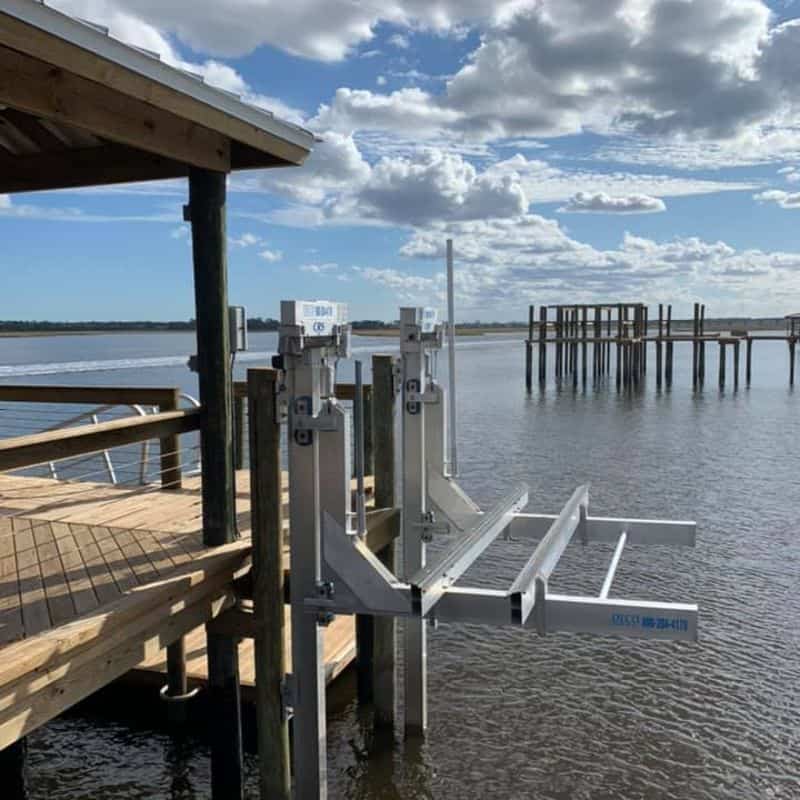 Aluminum boat lift with twin motor boxes mounted at a dock corner, old pilings across the water