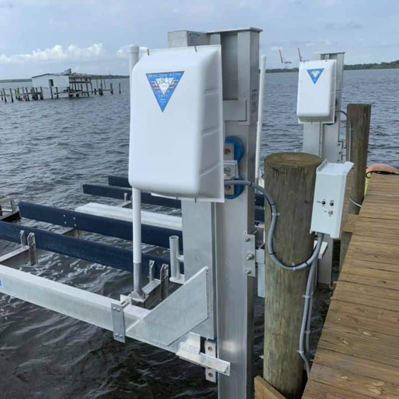Close view of a boat lift's white motor covers, control box and conduit on a wood dock