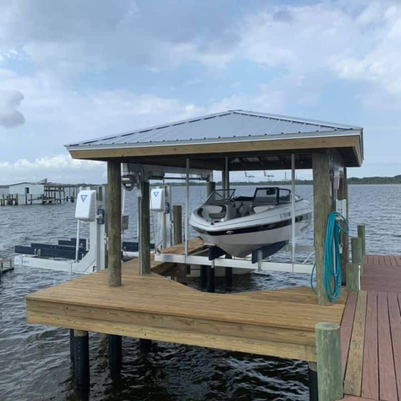 White bowrider raised on a lift under a hip-roof boathouse with a wraparound wood deck