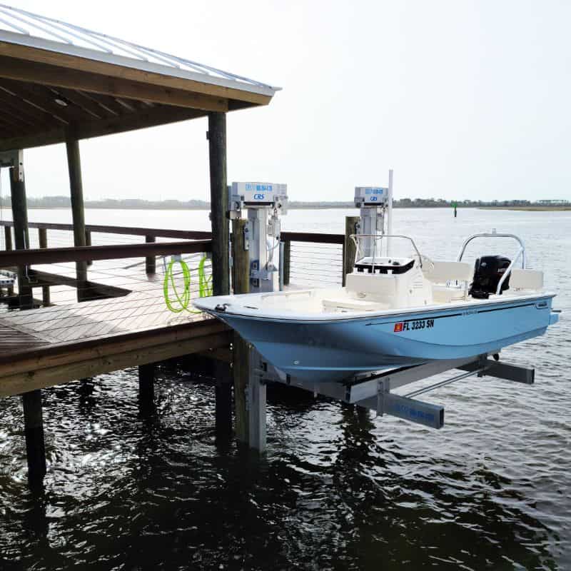 Light blue center console bay boat on an aluminum lift beside a covered dock