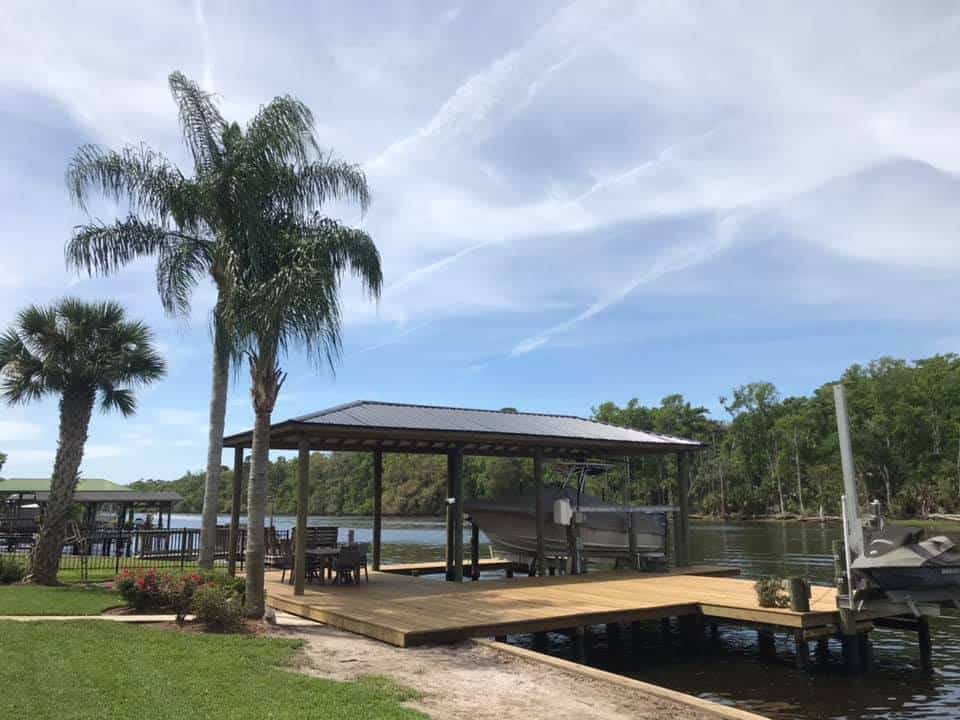 Open boathouse with metal roof shelters a boat on a lift beside a wooden dock