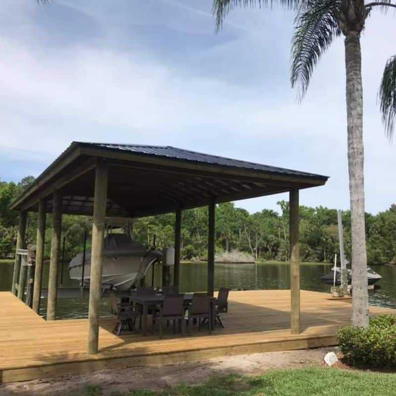 Open-sided boathouse over a river, patio dining set on the deck and a boat on the lift