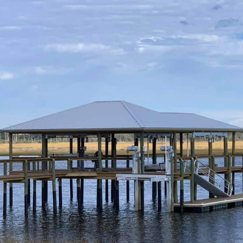 Large hip-roof boathouse on tall pilings with railed walkway, boat lift and aluminum ramp