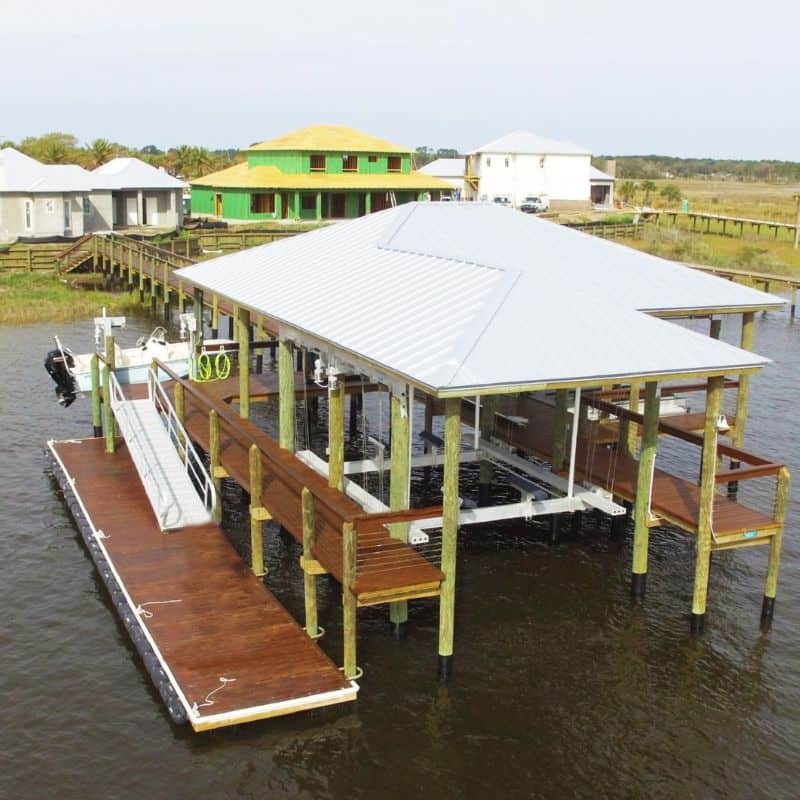Covered boathouse with metal roof, boat lifts, and a floating dock with gangway on open water