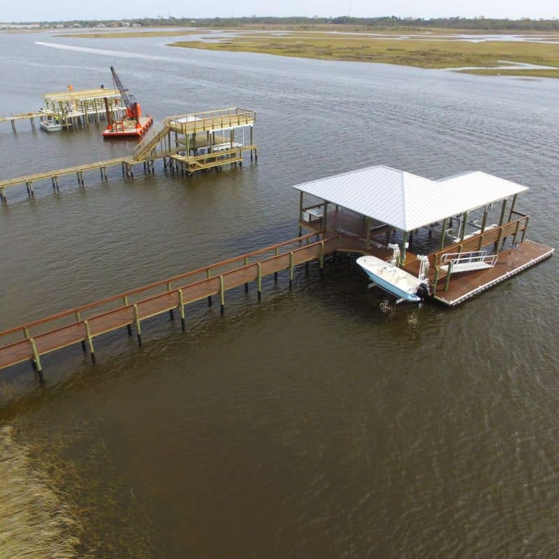 Aerial view of a long walkway leading to a covered boathouse and floating dock in a marsh creek