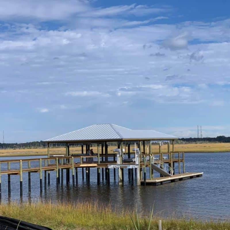 Boathouse with silver metal roof on pilings over marsh water, gangway down to a floating dock