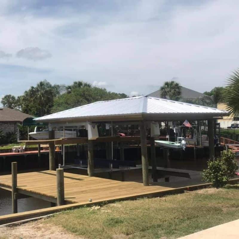 Backyard boathouse with white metal roof over two lifted boats beside a new wood dock