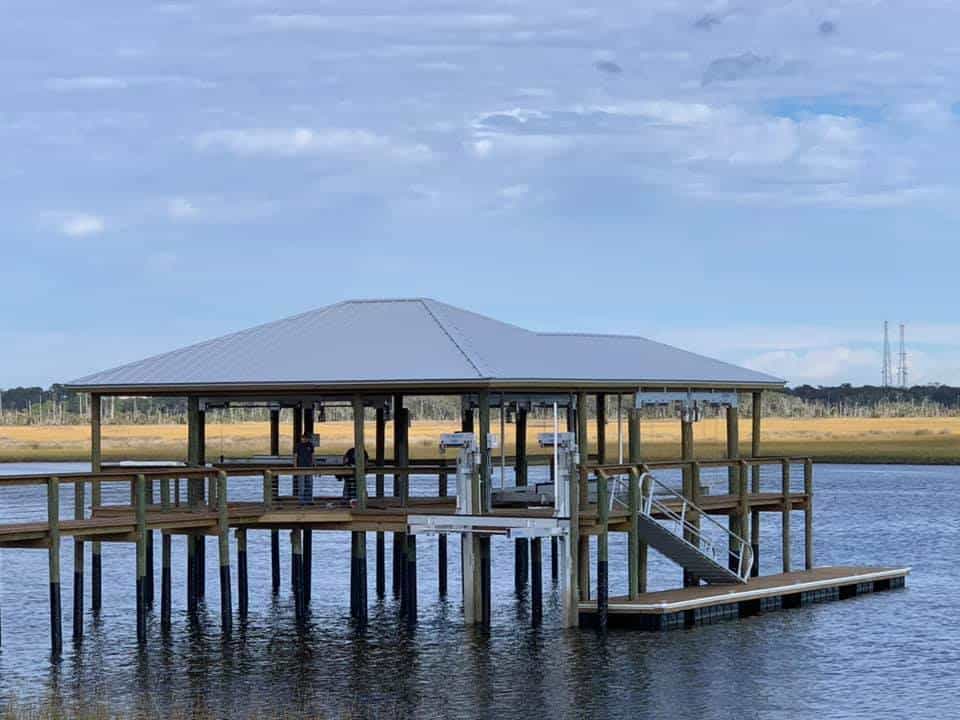 Boathouse with hip metal roof on pilings over water, gangway down to a floating dock
