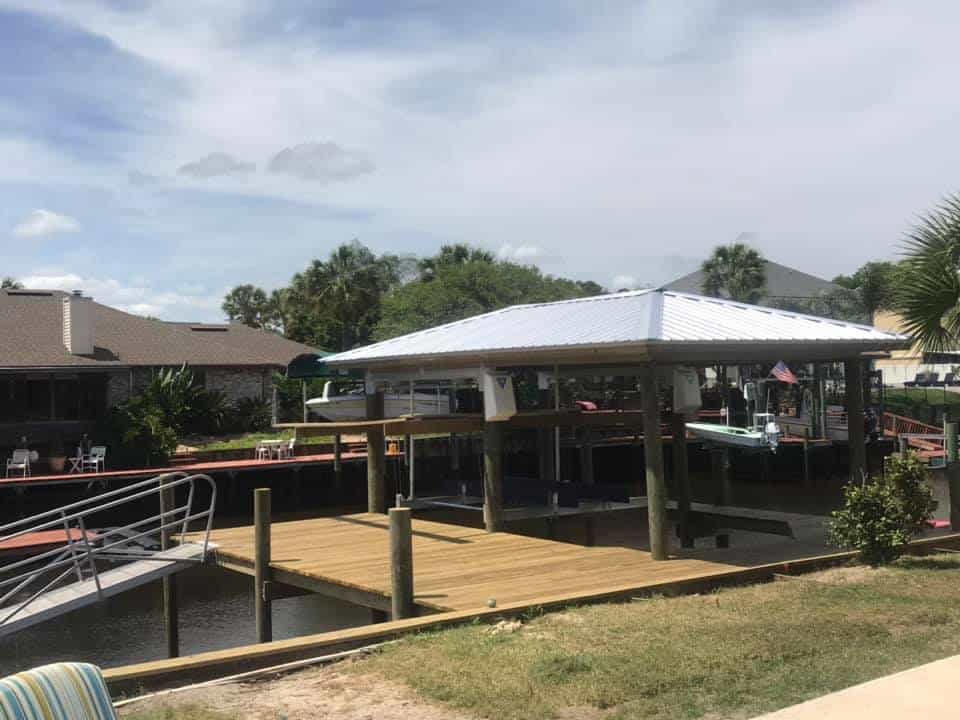 Boathouse with white metal roof sheltering two boats on lifts, wood dock in the foreground