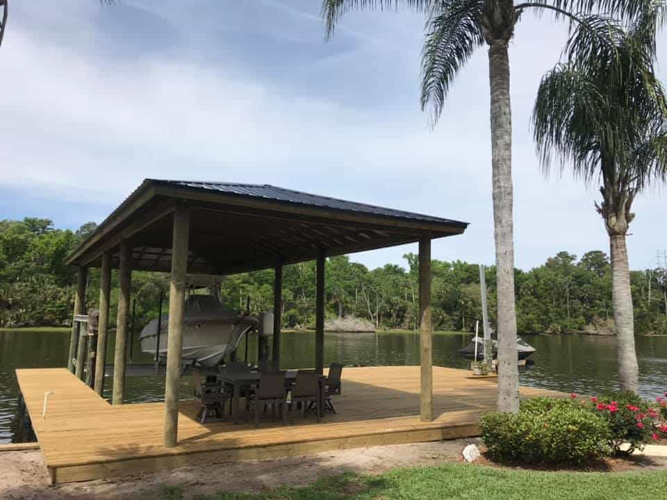 Riverside boathouse with dark roof and wide plank deck, center console on the lift and patio table