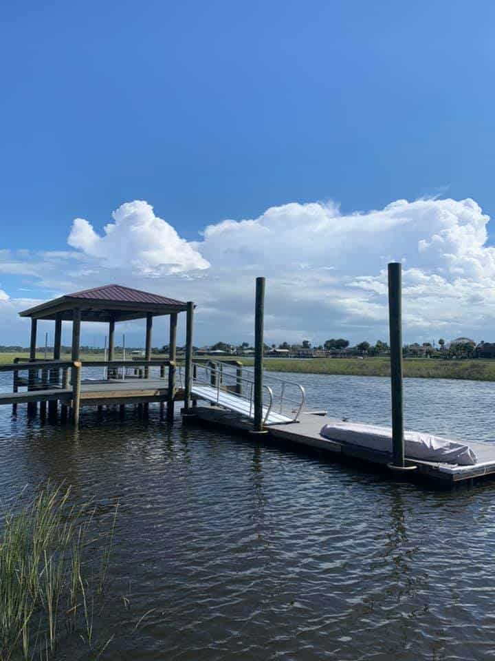 Covered dock with red roof joined by a railed gangway to a floating dock on calm marsh water