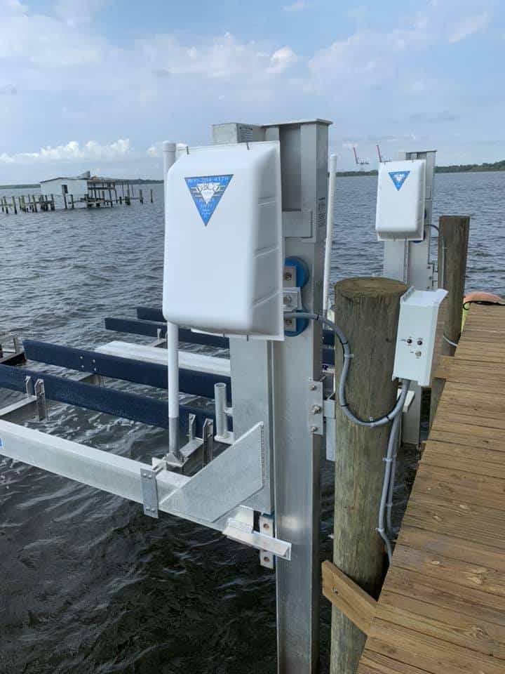 Boat lift cradle and white motor covers mounted along a wood dock, wiring run to a control box