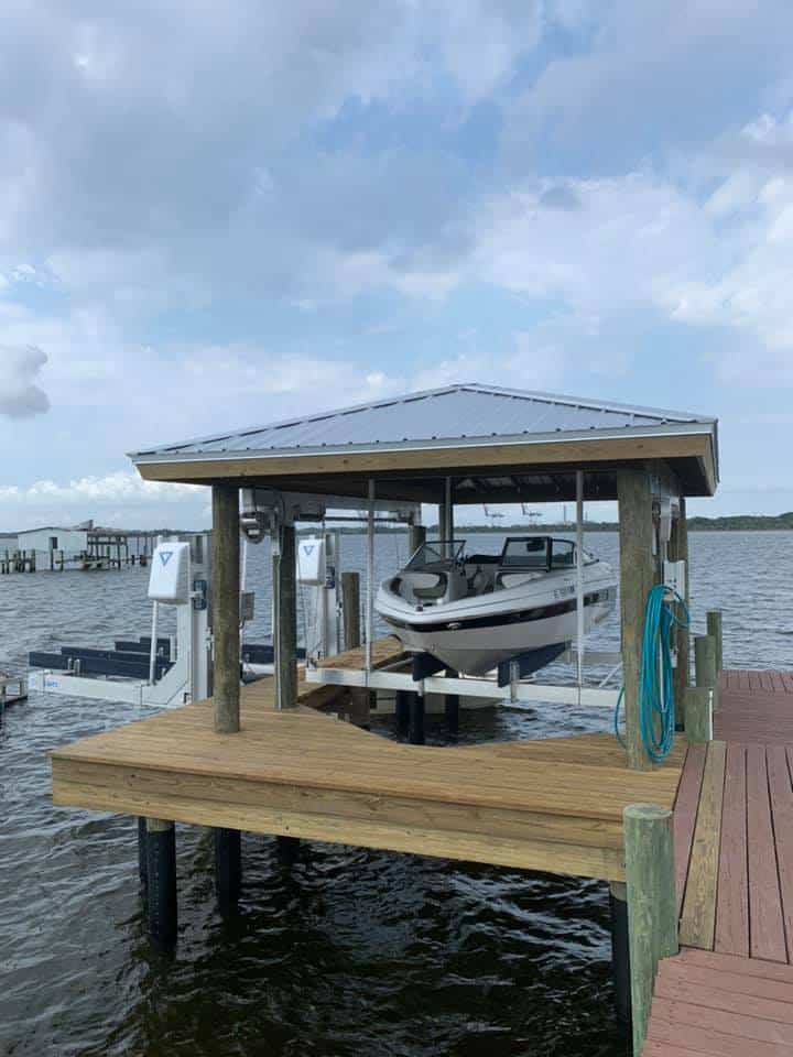 White speedboat raised on a covered boat lift above the water beside a wooden dock