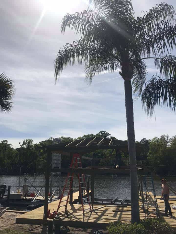 Boathouse frame with bare roof rafters under construction over water, ladders and a worker nearby